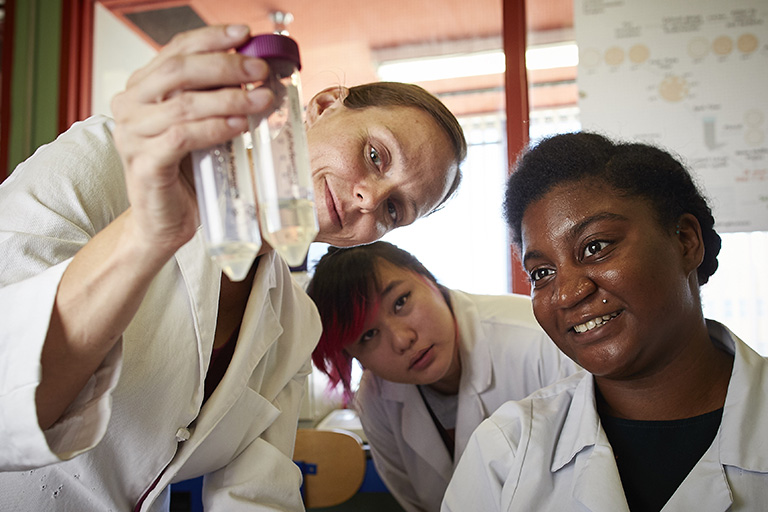 alt="Group of student workers examining liquid inside of beakers"