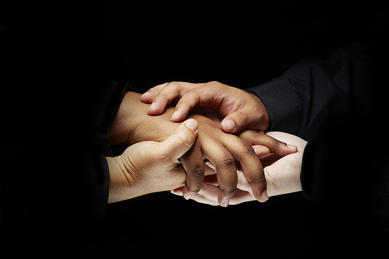 Close up of two people holding hands with dark background.